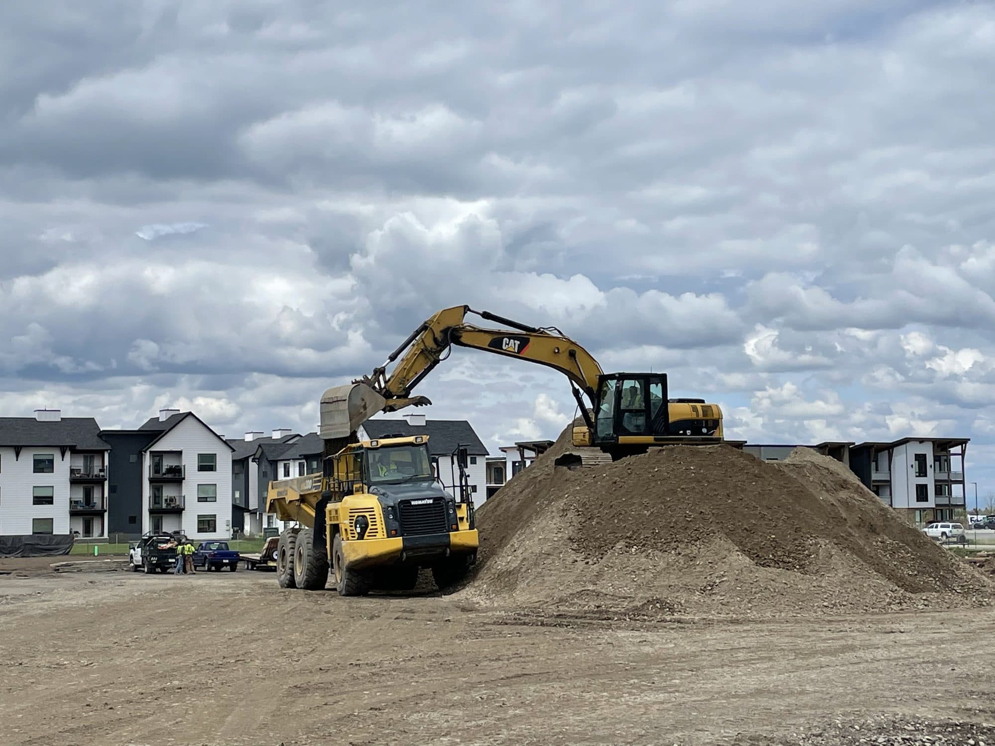 Excavator loading a haul truck on a dirt stockpile under a cloudy sky