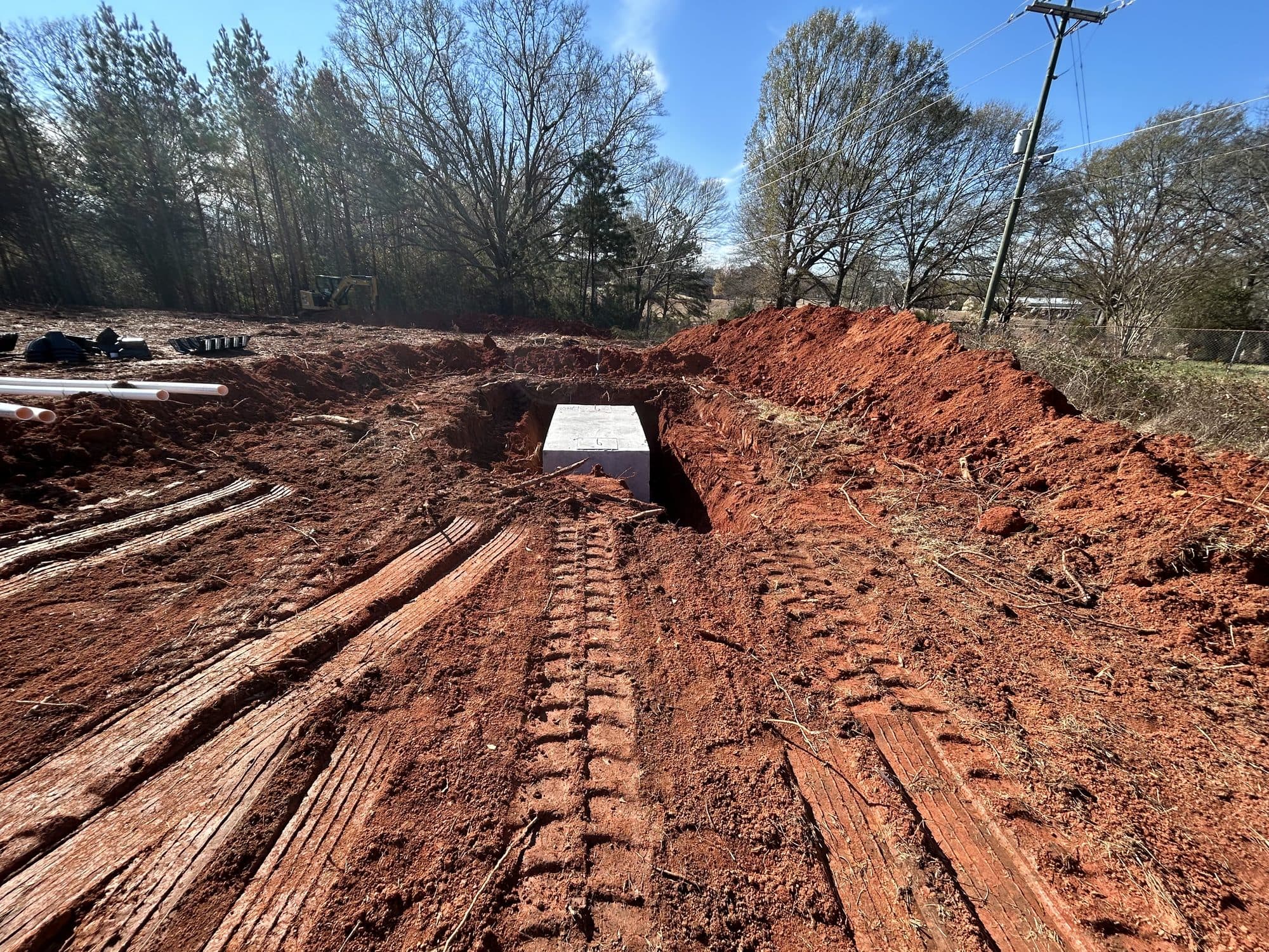 Concrete septic tank set in place in a freshly excavated trench, with equipment track marks in the clay