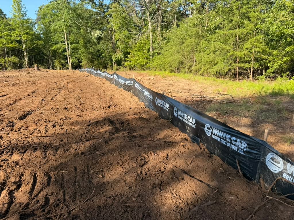 Silt fence staked along the toe of a freshly graded bank of red clay