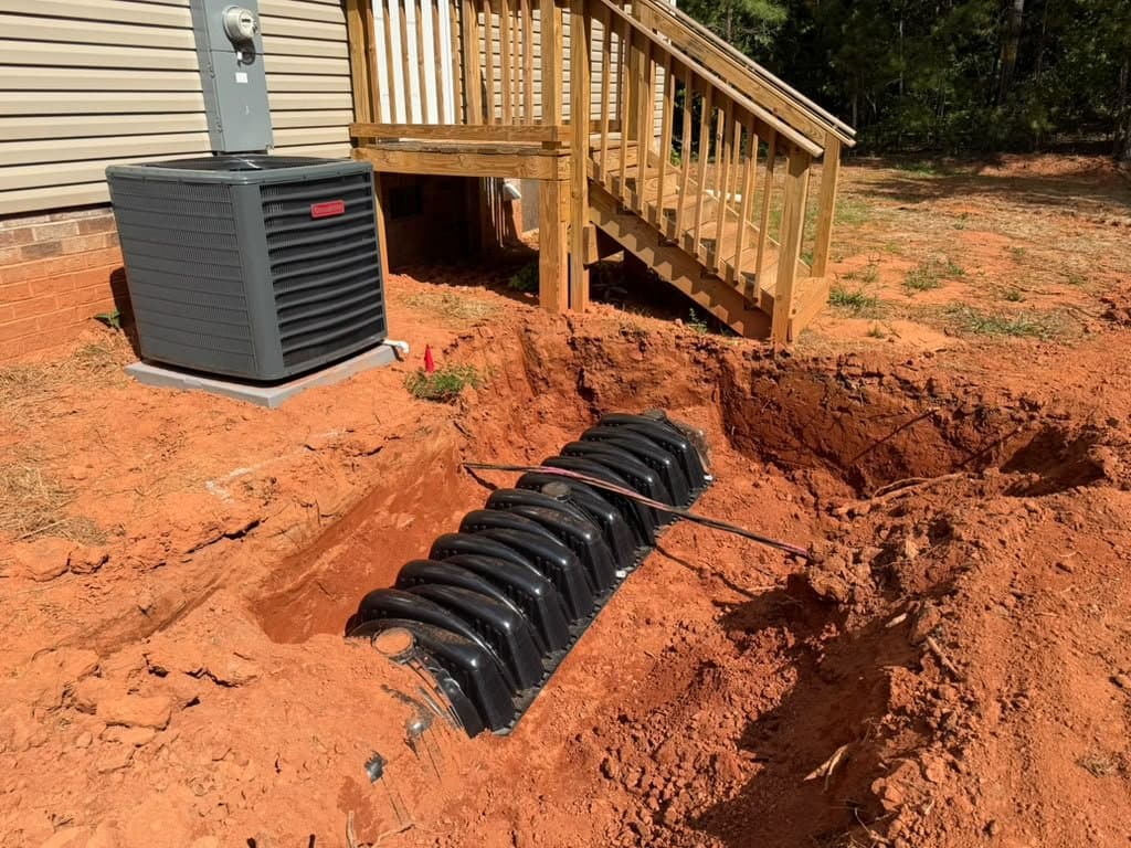 Plastic septic chambers set in an open trench alongside an existing home, beside the air conditioning unit and a new deck