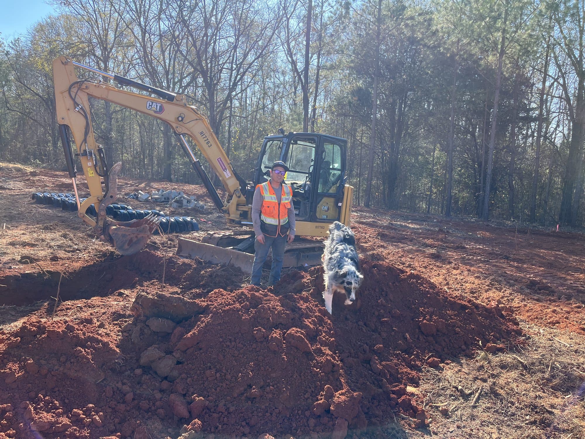 Joseph Caddel and his dog Bridger on a job site in front of a CAT mini excavator
