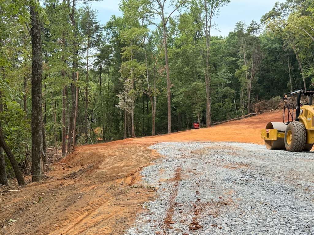 Compactor roller on a freshly built gravel access road through a wooded site