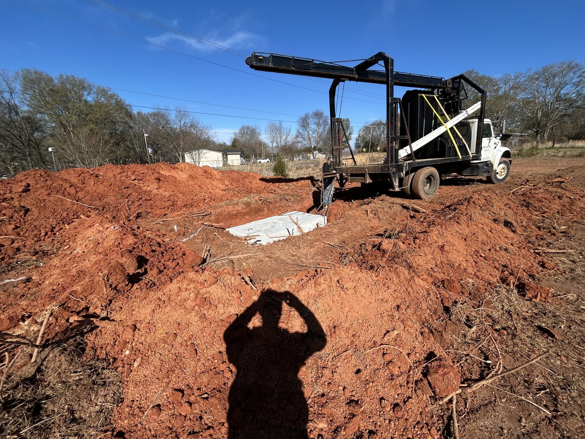 Boom truck lowering a concrete septic tank into an excavated pit